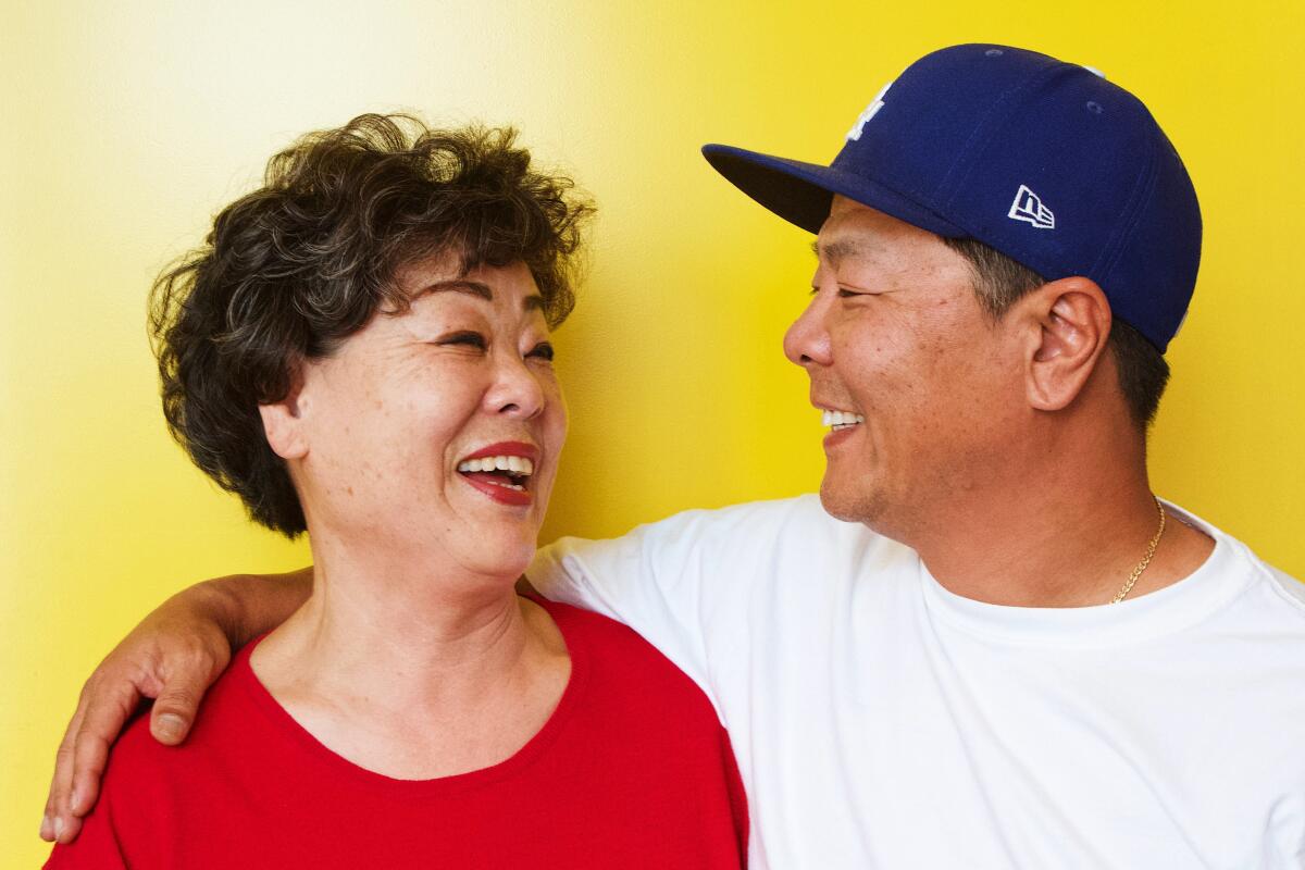 A man with his arm around his mother, both smiling as they face each other.