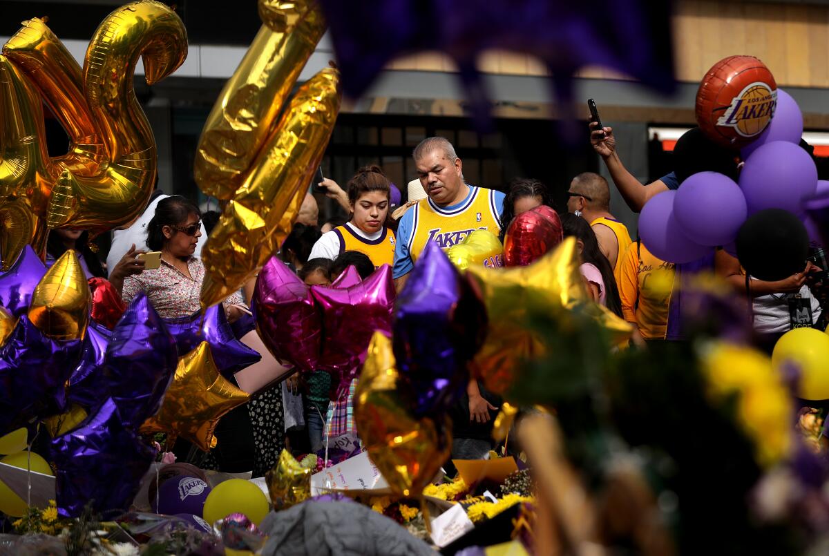 A man and woman in Lakers jerseys can be seen through purple and gold balloons among a crowd at L.A. Live.
