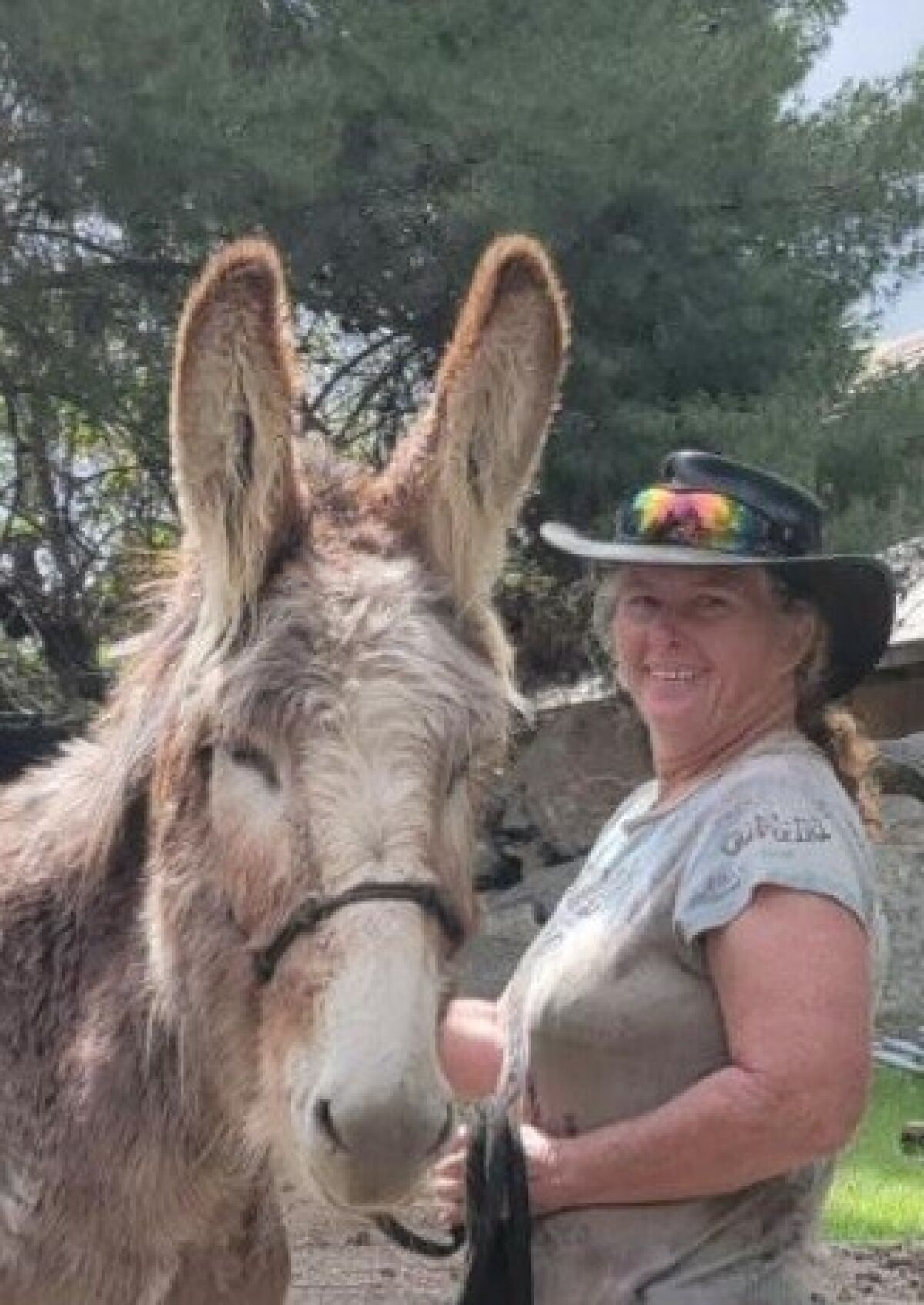 A woman in a cowboy hat stands next to a donkey.