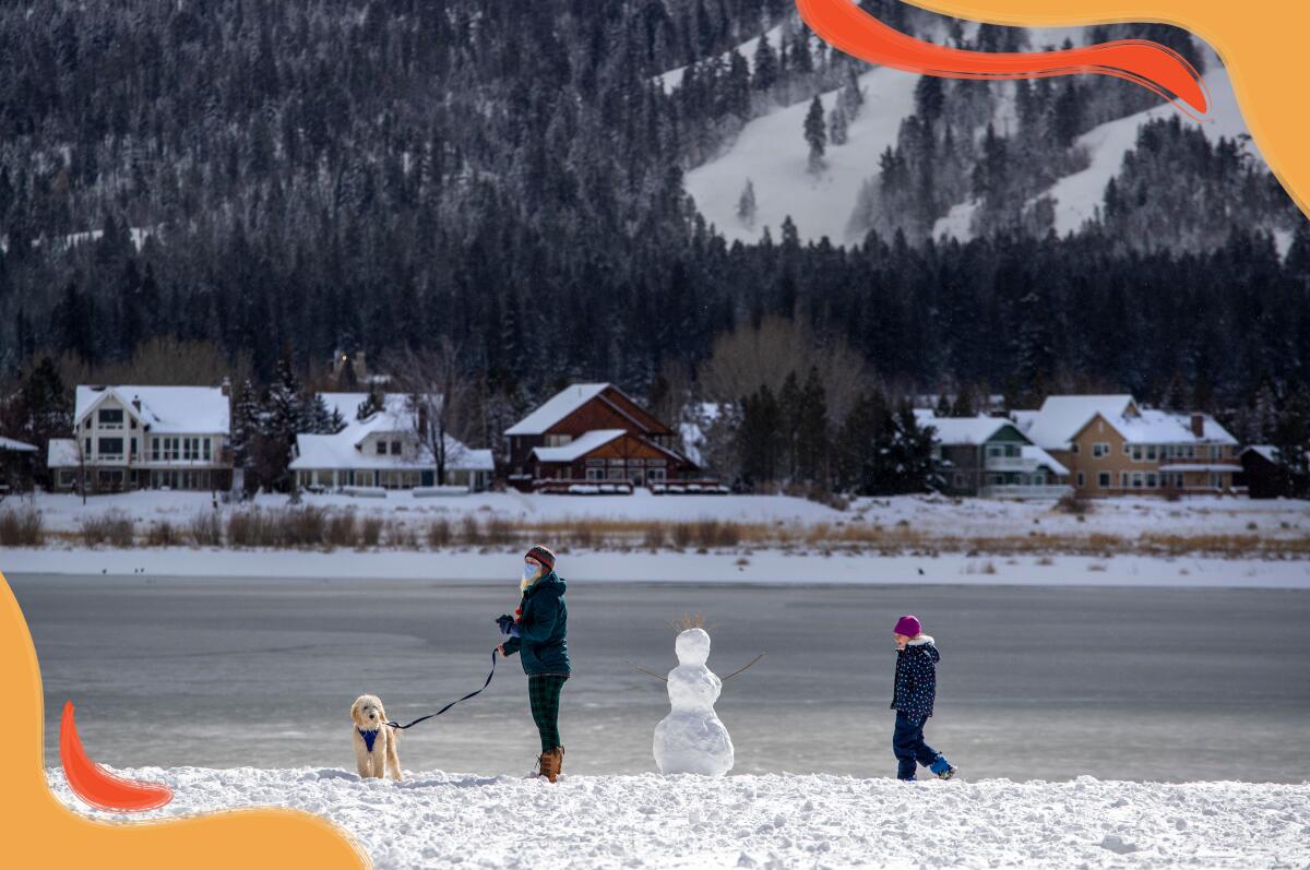 Mujer y niño en la orilla de lago nevado con un perro y muñeco de nieve