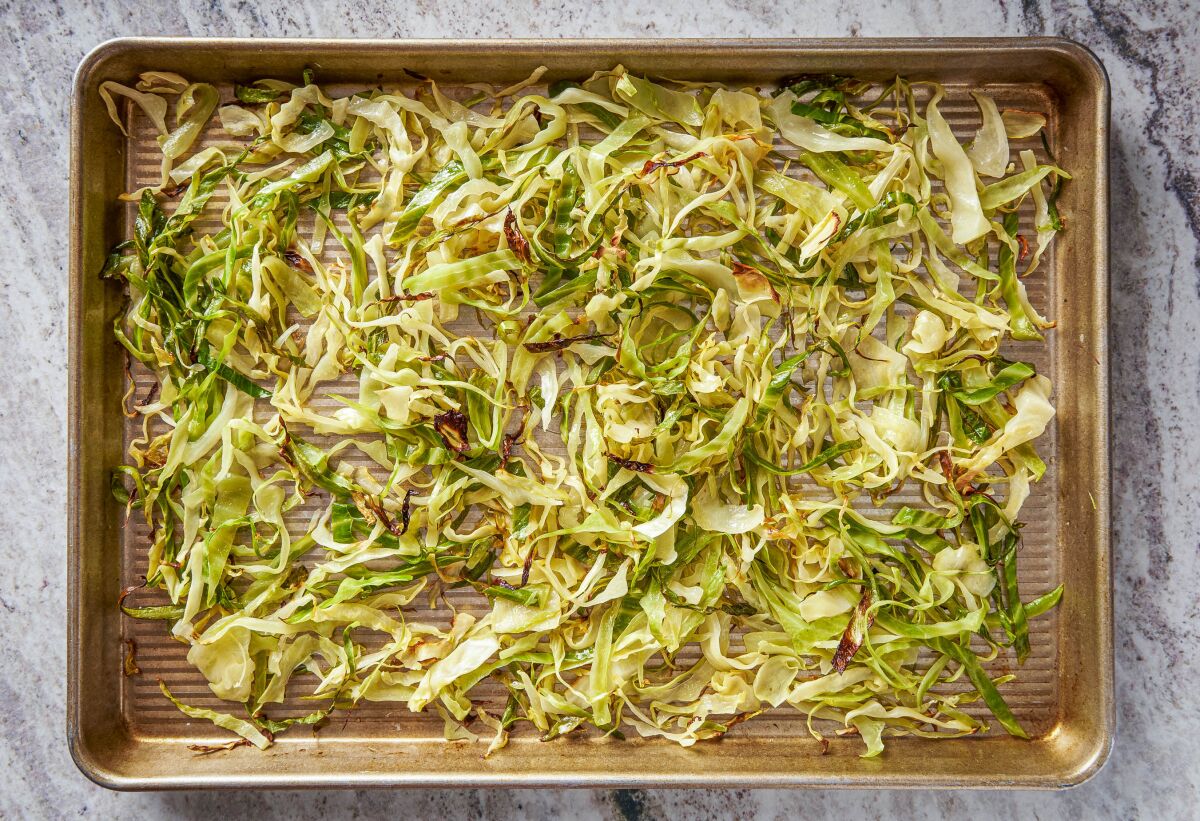 Strips of roasted cabbage lie on a large, rimmed baking sheet. 