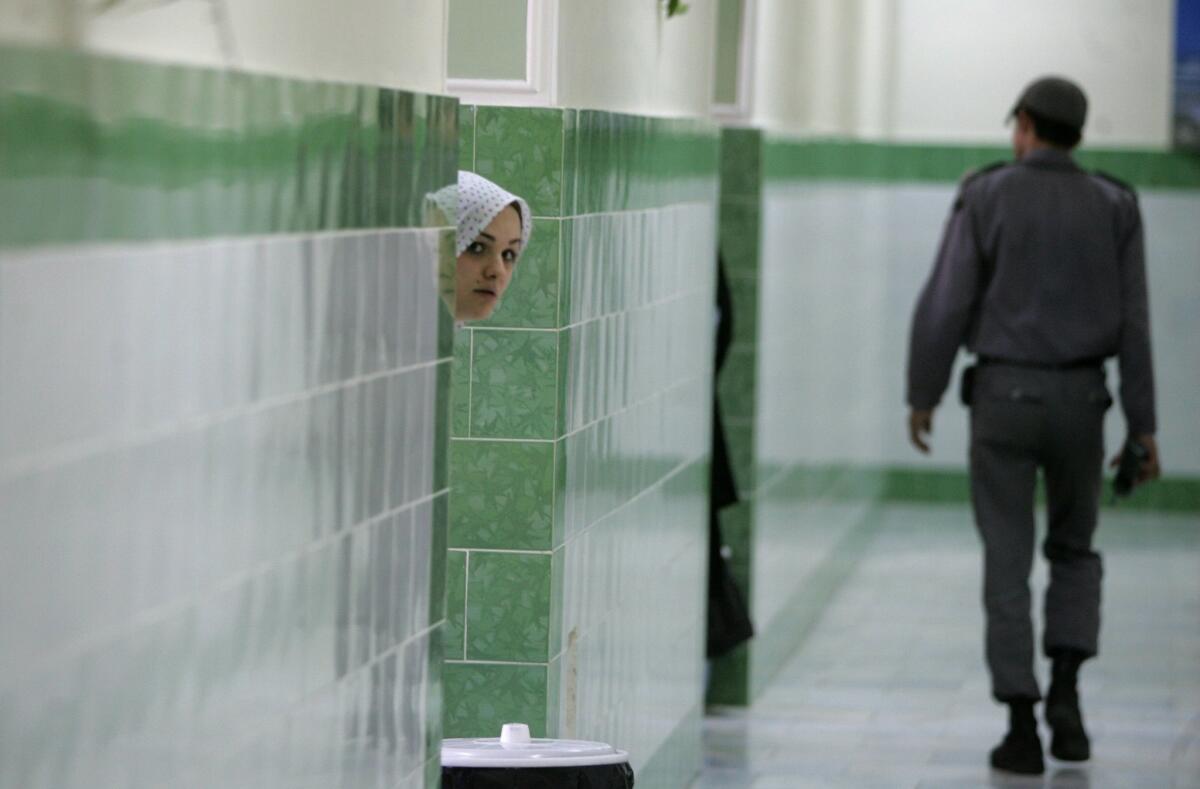 An inmate peers out as a guard passes in the female section of Evin Prison, north of Tehran, in June 2006.