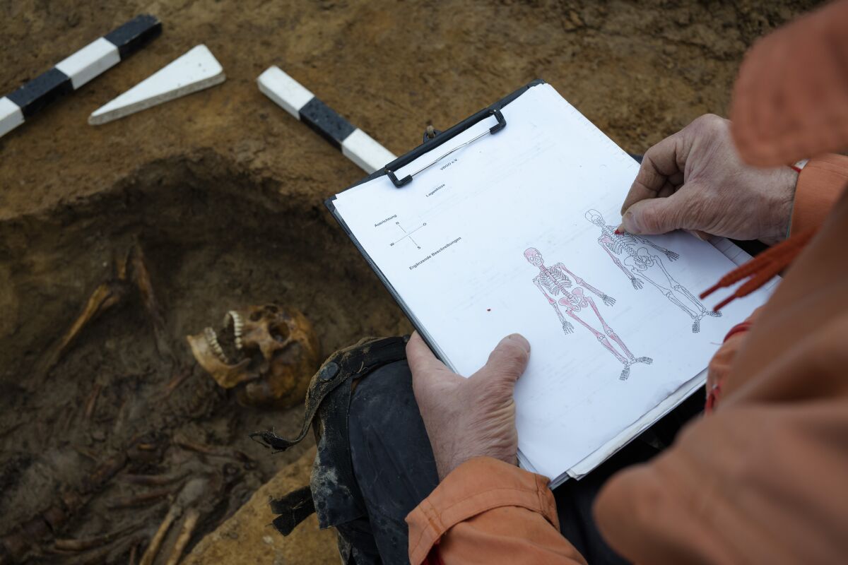 An excavation technician makes a note on a diagram to confirm that remains from World War II belong to a single person.