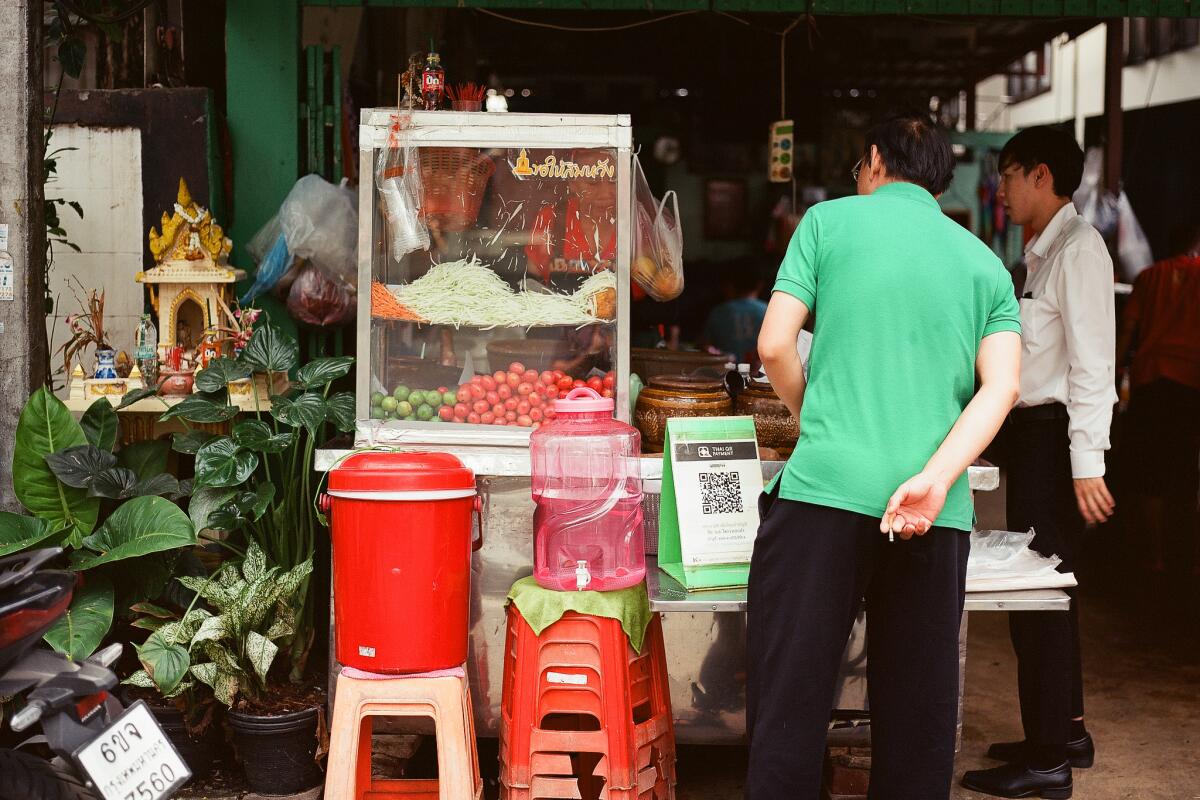 People stand in front of a food stand in Bangkok.