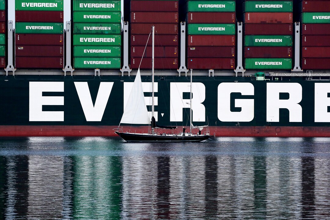 A tour boat is dwarfed by a ship and stacks of cargo containers