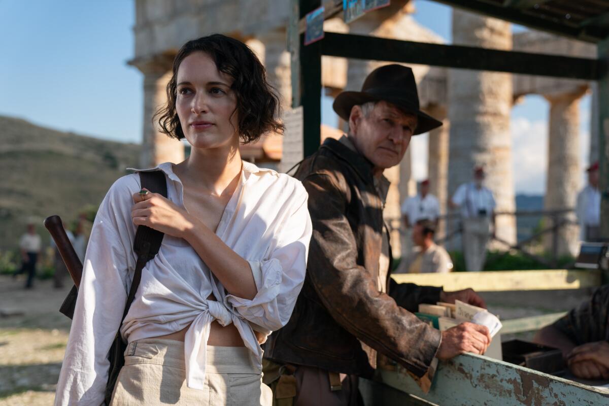 A woman next to a man in a fedora in front of an ancient ruin.