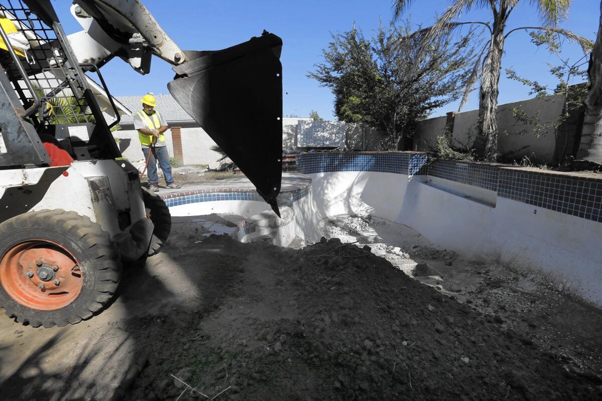Andrew Casillas uses a loader to fill in a swimming pool while Jeremy Chavez waters down the dirt to help solidify it in a Yorba Linda backyard.