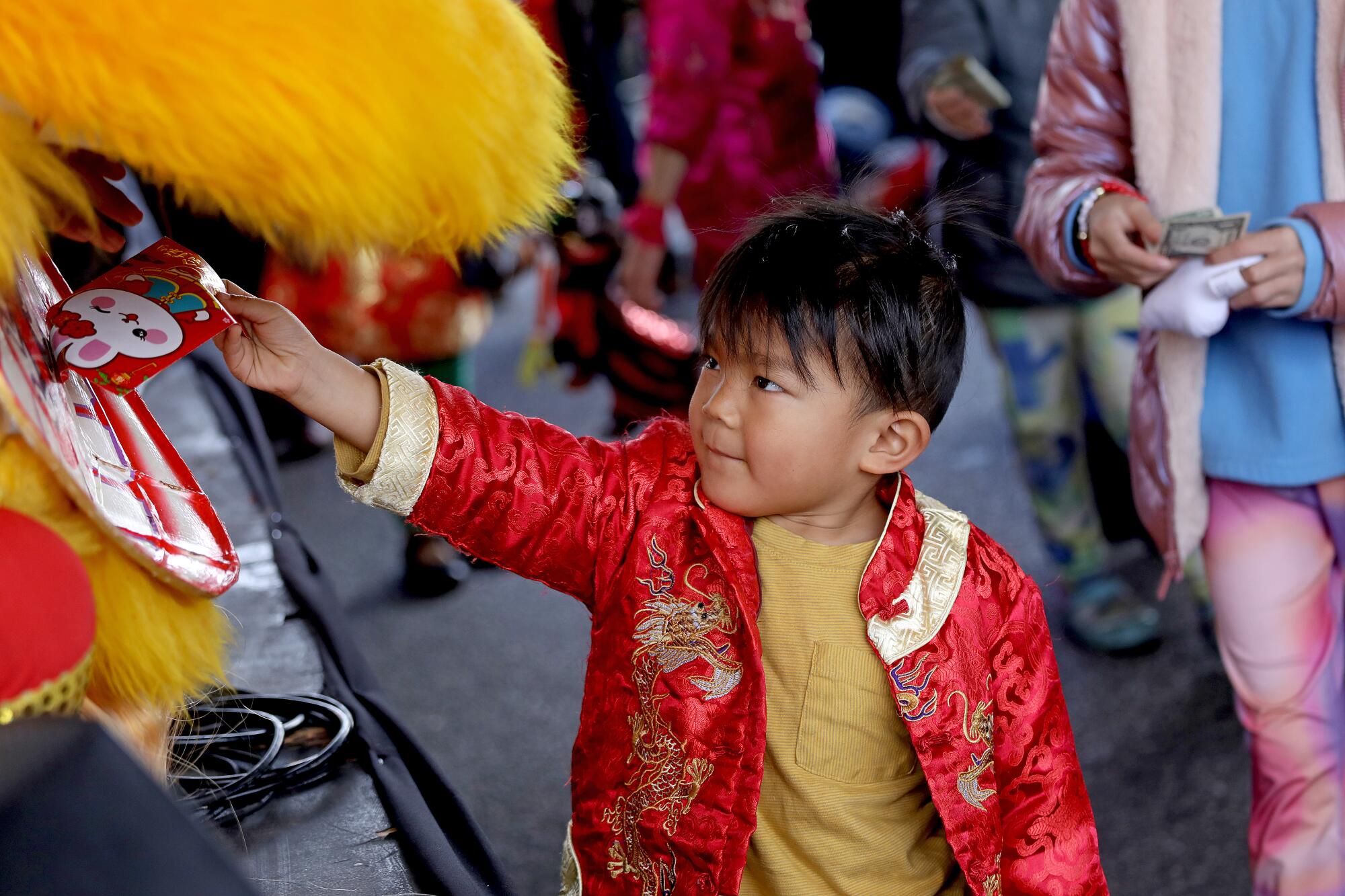 A young boy places a New Year's envelope into the mouth of a dancer at the Alhambra Lunar New Year Festival.