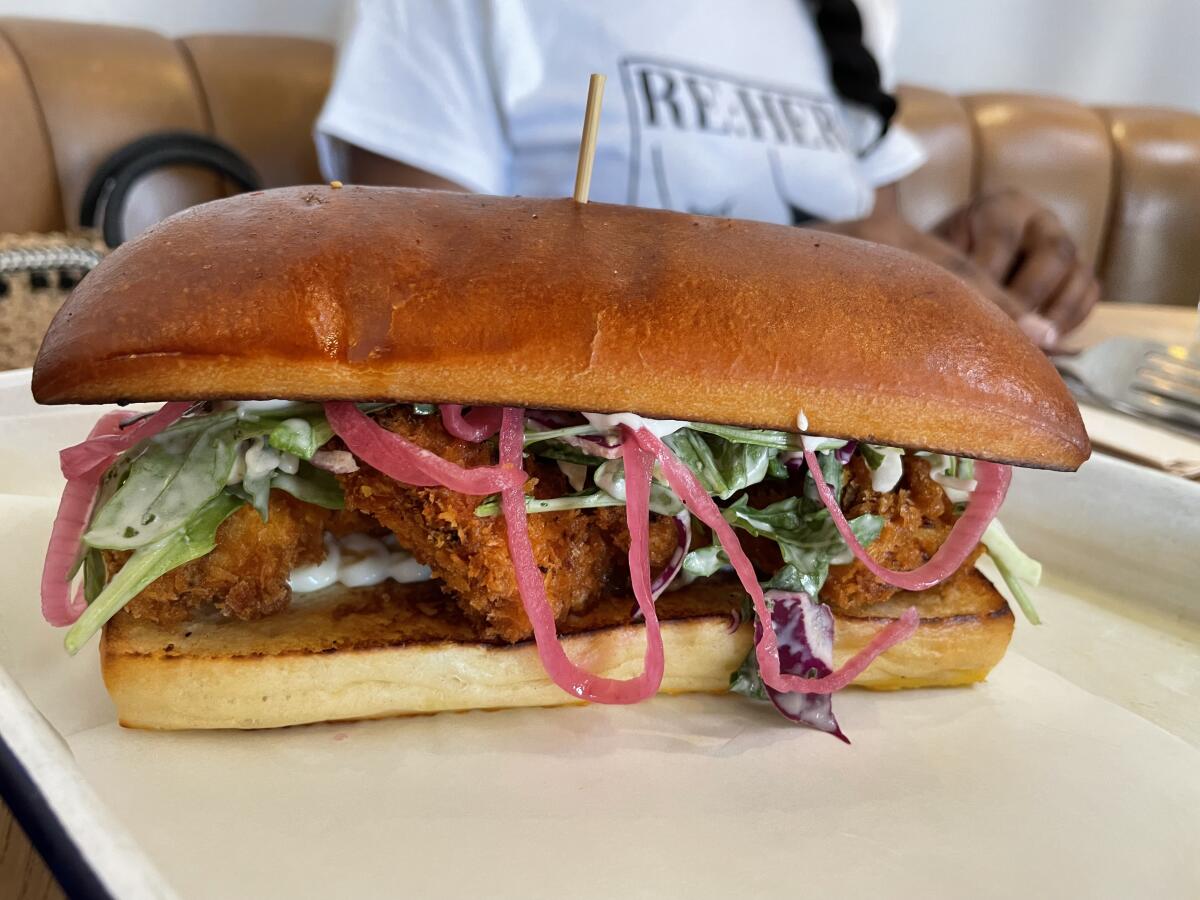 A sandwich with fried chicken and pickled onions on a restaurant table.