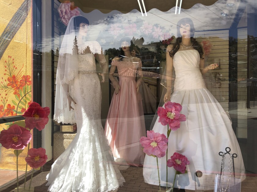 FILE - Mannequins in wedding gowns are seen in a window display on March 15, 2021, at a bridal store in Nogales, Ariz. The holidays are a popular time to get engaged, and that means many couples are diving into 2022 by touring wedding venues, researching vendors and carefully crafting guest lists. Planning a wedding can be a time that’s filled with emotions, expectations and the pressure to create a perfect event — all of that combined makes it far too easy to overspend. (AP Photo/Suman Naishadham)