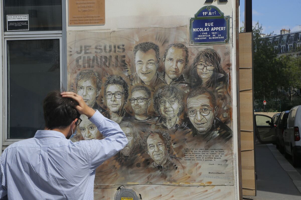 A man wearing a protective face mask as a precaution against the coronavirus looks on a painting by French street artist Christian Guemy, a.k.a. 'C215' in Paris Wednesday, Sept. 2, 2020, in tribute to the members of the satirical newspaper Charlie Hebdo attack by jihadist gunmen in January 2015. Thirteen men and a woman go on trial Wednesday over the 2015 attacks against a satirical newspaper and a kosher supermarket in Paris that marked the beginning of a wave of violence by the Islamic State group in Europe. Seventeen people and all three gunmen died during the three days of attacks in January 2015. (AP Photo/Michel Euler)