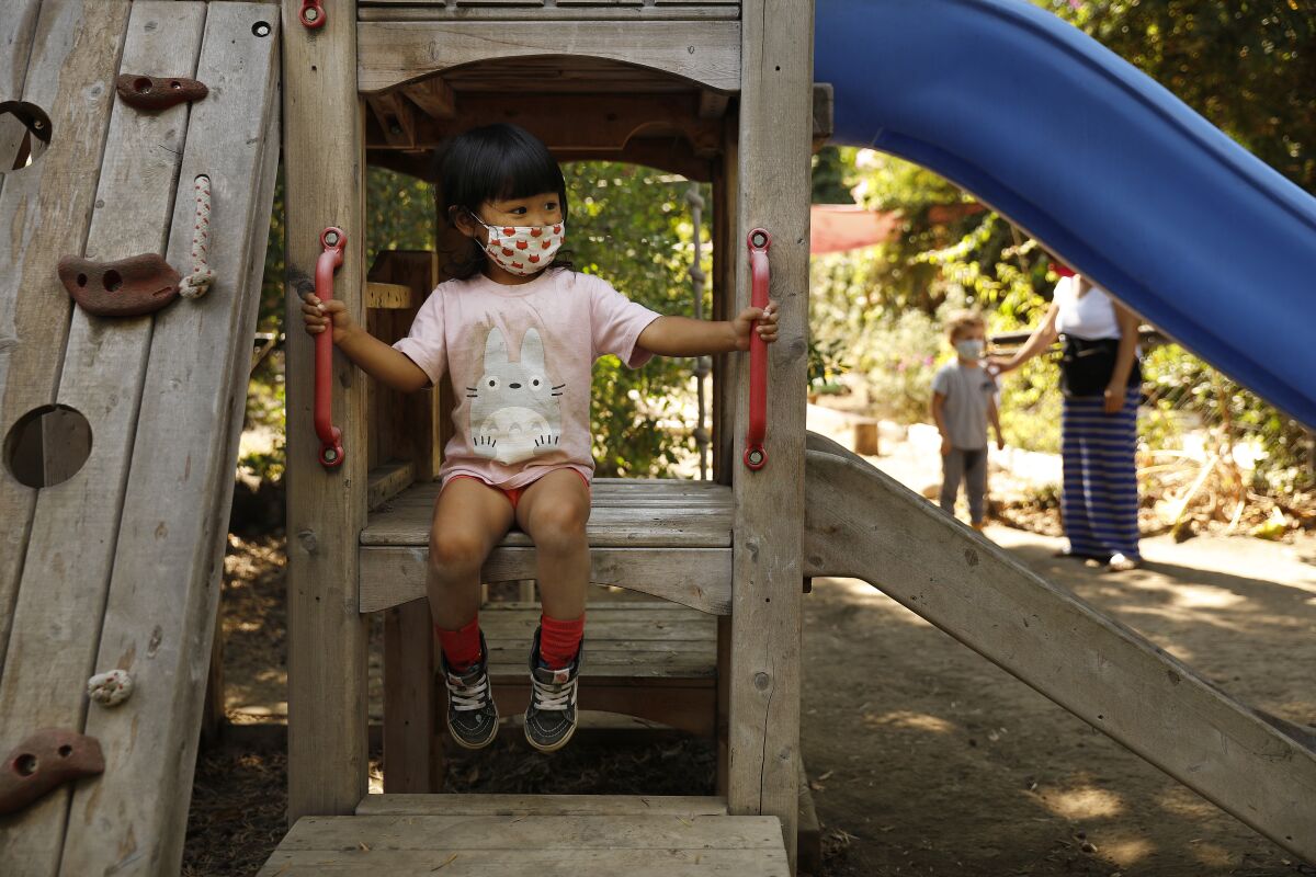 Masked preschool student sitting on outdoor playground equipment