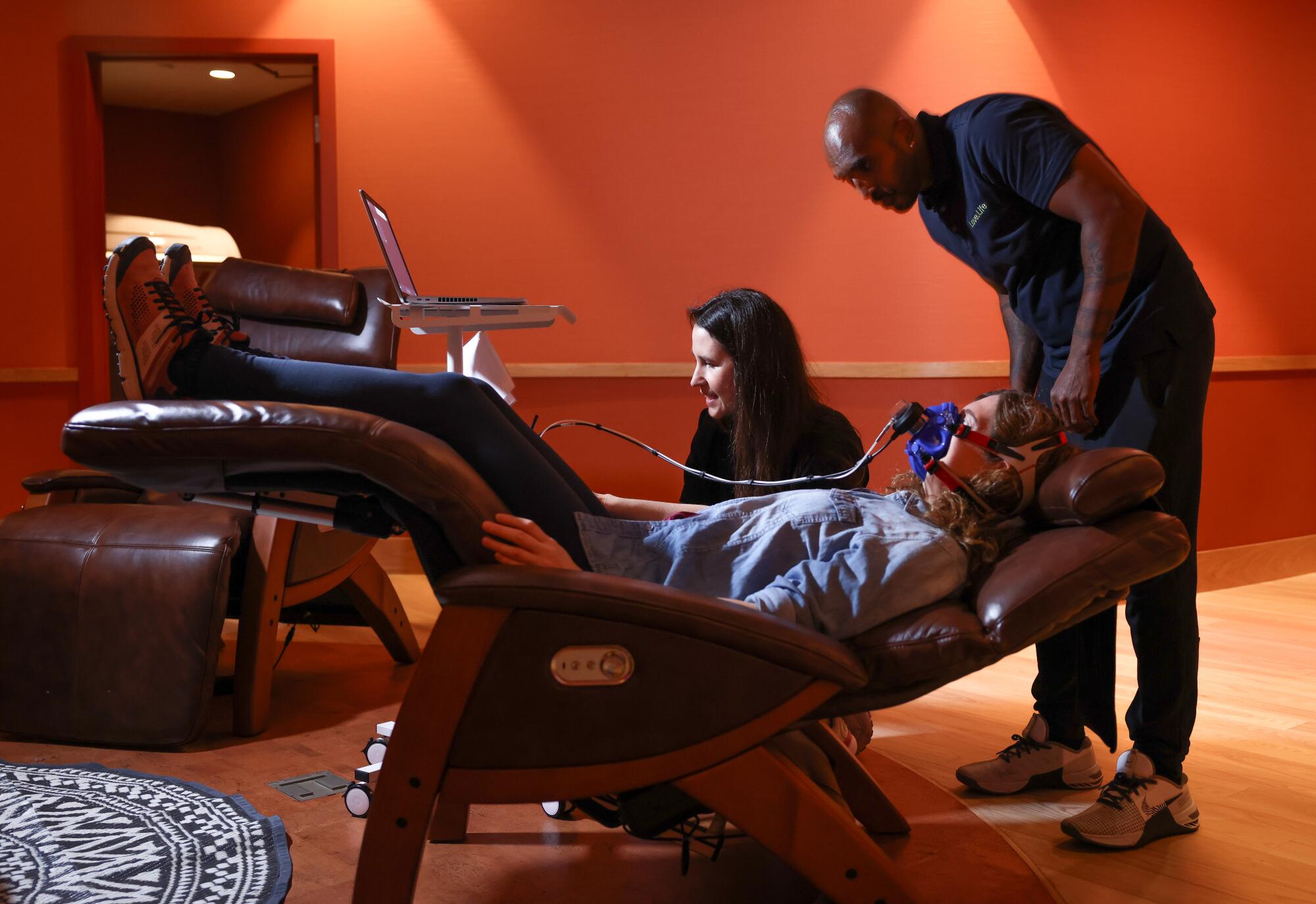 A woman reclines with two people performing various tests on her