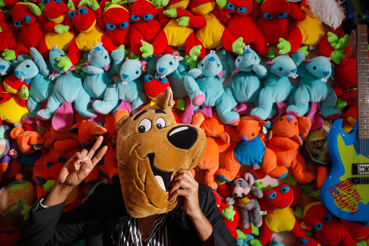 Enrique Tena Padilla, seated before a wall of Beanie Babes, obscures his face with a Scooby Doo stuffed animal. 