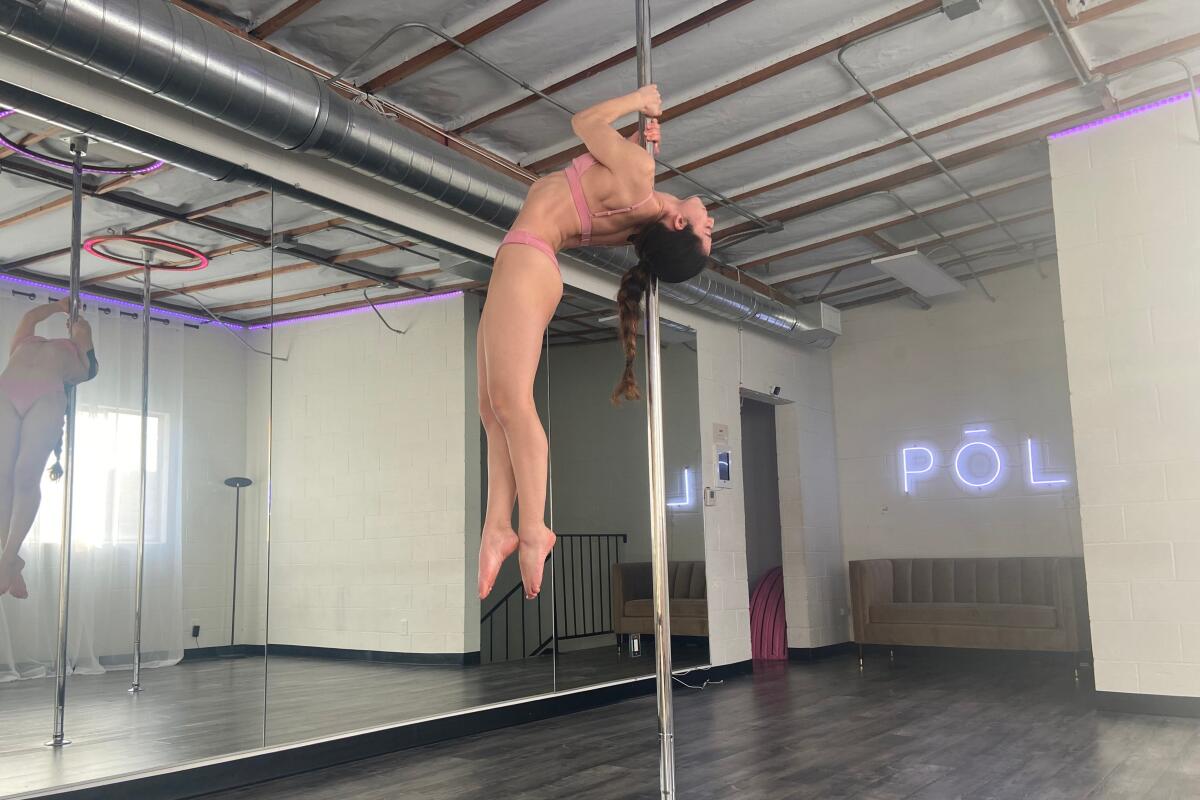 A woman pole-dancing before a mirrored wall, with POL spelled in neon on a facing wall