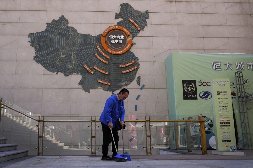 FILE - A cleaner sweeps near a map showing Evergrande development projects in China on a wall in an Evergrande city plaza in Beijing on Sept. 21, 2021. A Chinese real estate developer whose struggle to manage more than $300 billion in debt rattled global financial markets announced a long-awaited plan Thursday, March 23, 2023, to restructure what it owes to foreign bondholders. (AP Photo/Andy Wong, File)