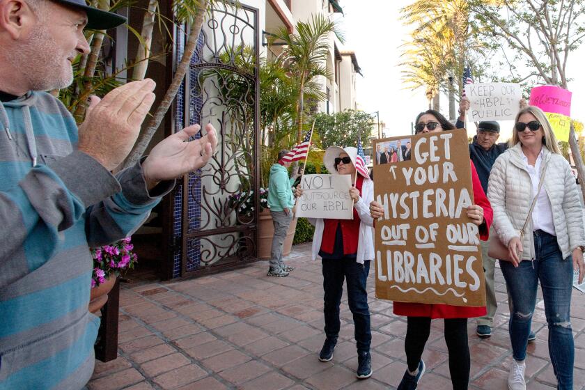 Eric Silkenson, left, applauds for over 100 people who march in protest of proposed plans to privatize the Huntington Beach libraries and create a children's book review board on Friday.