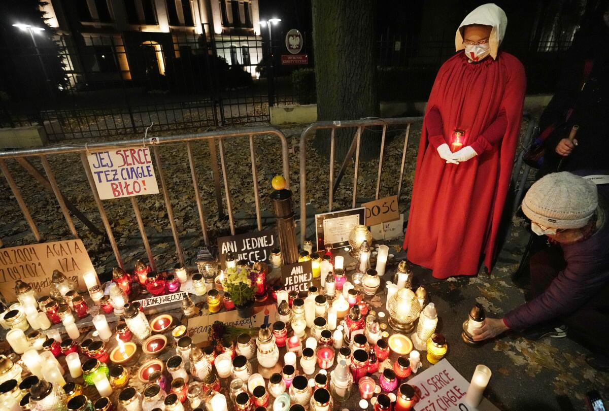 Candlelight vigil with a woman nearby dressed in a red outfit and white head covering and gloves.