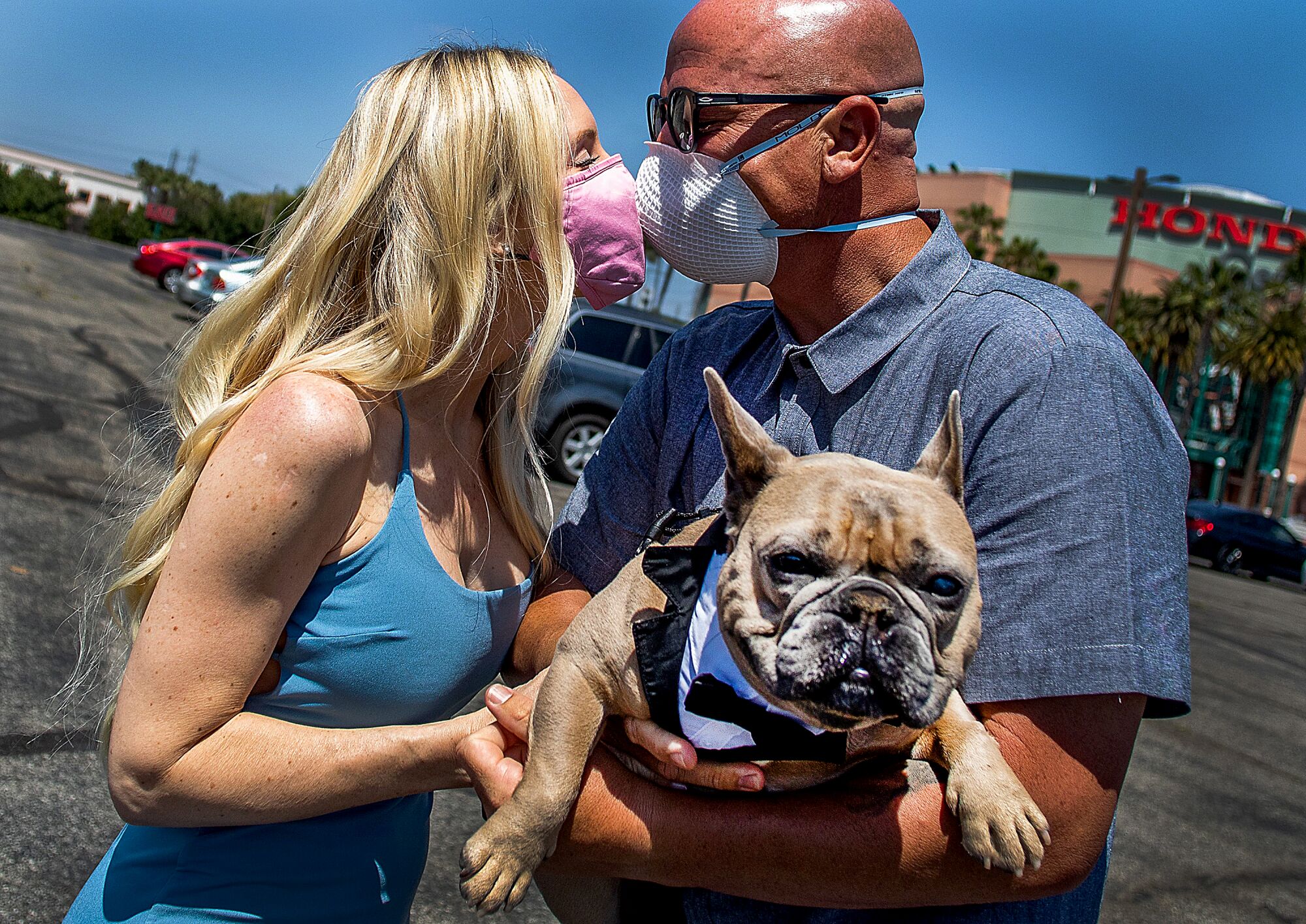 CALIFORNIA, USA: Chad Robbins and Tracey Robbins (R) kiss wearing face masks and holding their dog Huggy after their wedding ceremony officiated by a clerk recorder at the Honda Center parking lot on April 21, 2020 in Anaheim, California. - The County of Orange Clerk Recorder employees implemented a variety of social distancing techniques to safely issue licenses and marry couples during the novel coronavirus pandemic.