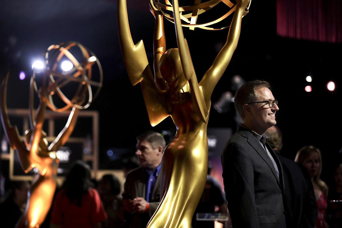 A man on a stage with larger-than-life Emmy statuettes