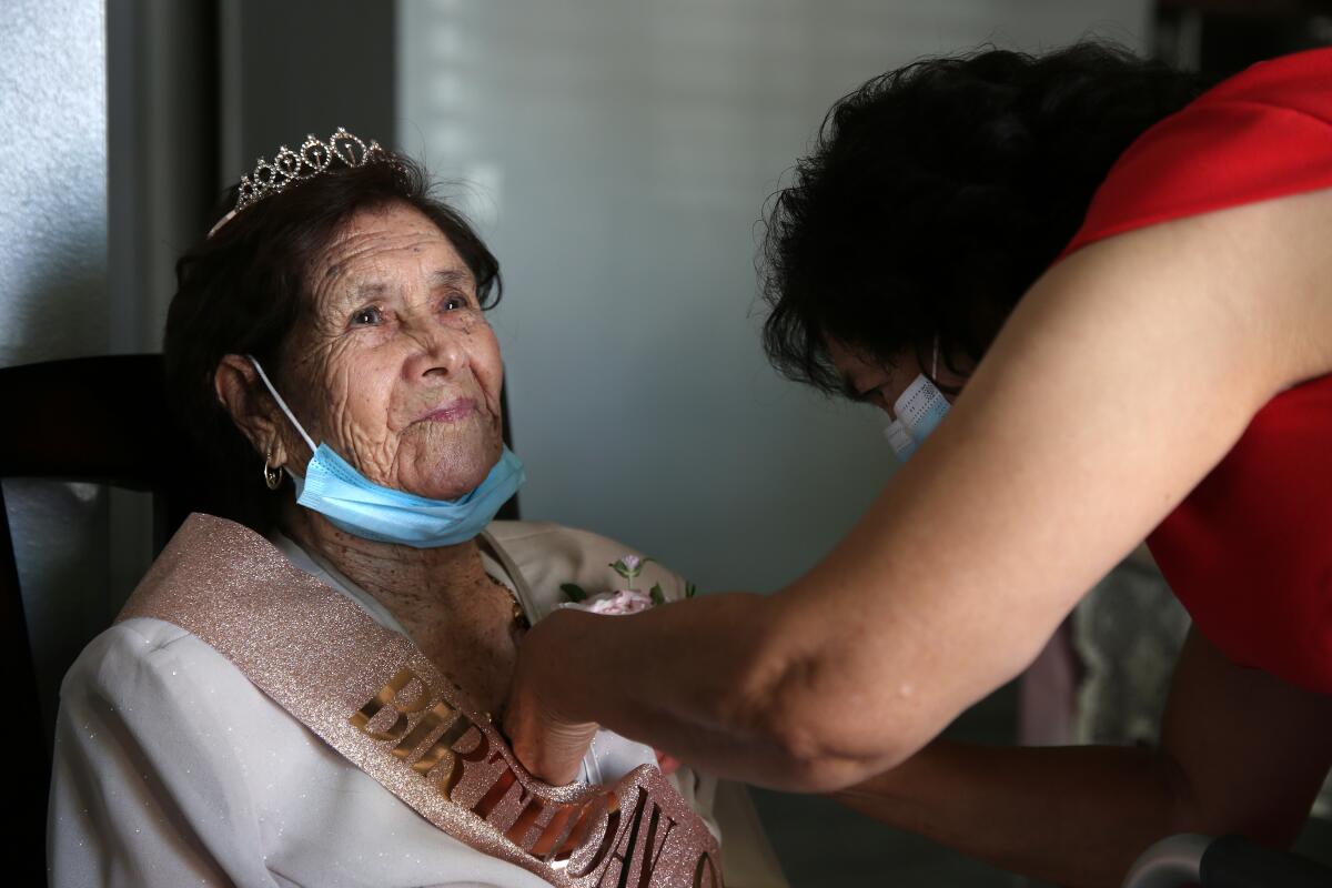 Paula Cabrera places a flower pin on the coat of her mother, who wears a sash and tiara