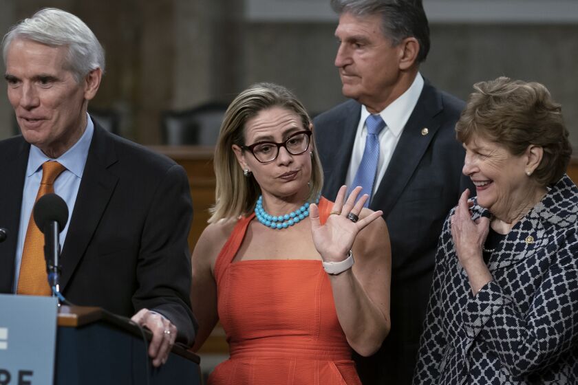 FILE- Sen. Kyrsten Sinema, D-Ariz., center, gestures during a news conference at the Capitol in Washington, Wednesday, July 28, 2021, while working on a bipartisan infrastructure bill with, from left, Sen. Rob Portman, R-Ohio, Sen. Joe Manchin, D-W.Va., and Sen. Jeanne Shaheen, D-N.H. Though elected as a Democratic, Sinema announced Friday, Dec. 9, that she has registered as an independent, but she does not plan to caucus with Republicans, ensuring Democrats will retain their narrow majority in the Senate. (AP Photo/J. Scott Applewhite, File)