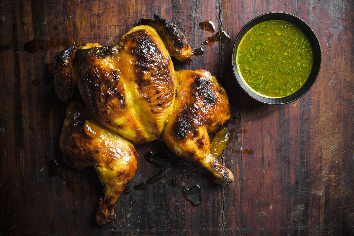 This image released by Milk Street shows a recipe for chutney-glazed spatchcocked chicken. Spatchcocking, or butterflying, involves cutting out a bird’s backbone so it can be flattened. This allows the chicken to brown evenly and helps the glaze stay put. Their simple glaze mixes tangy-sweet chutney with butter and turmeric. Citrus juice added to a portion of the glaze before cooking makes a bright dipping sauce. (Milk Street via AP)