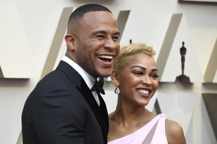 A man in a tuxedo and a woman in a pink, off-the-shoulder gown smile for cameras at the Oscars