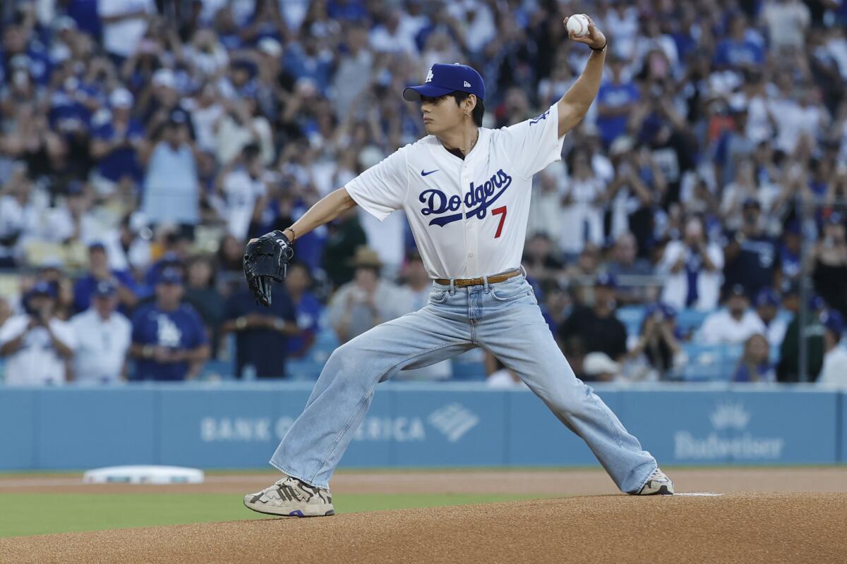 A Korean man in a Dodgers jersey and jeans throws from a pitcher's mound