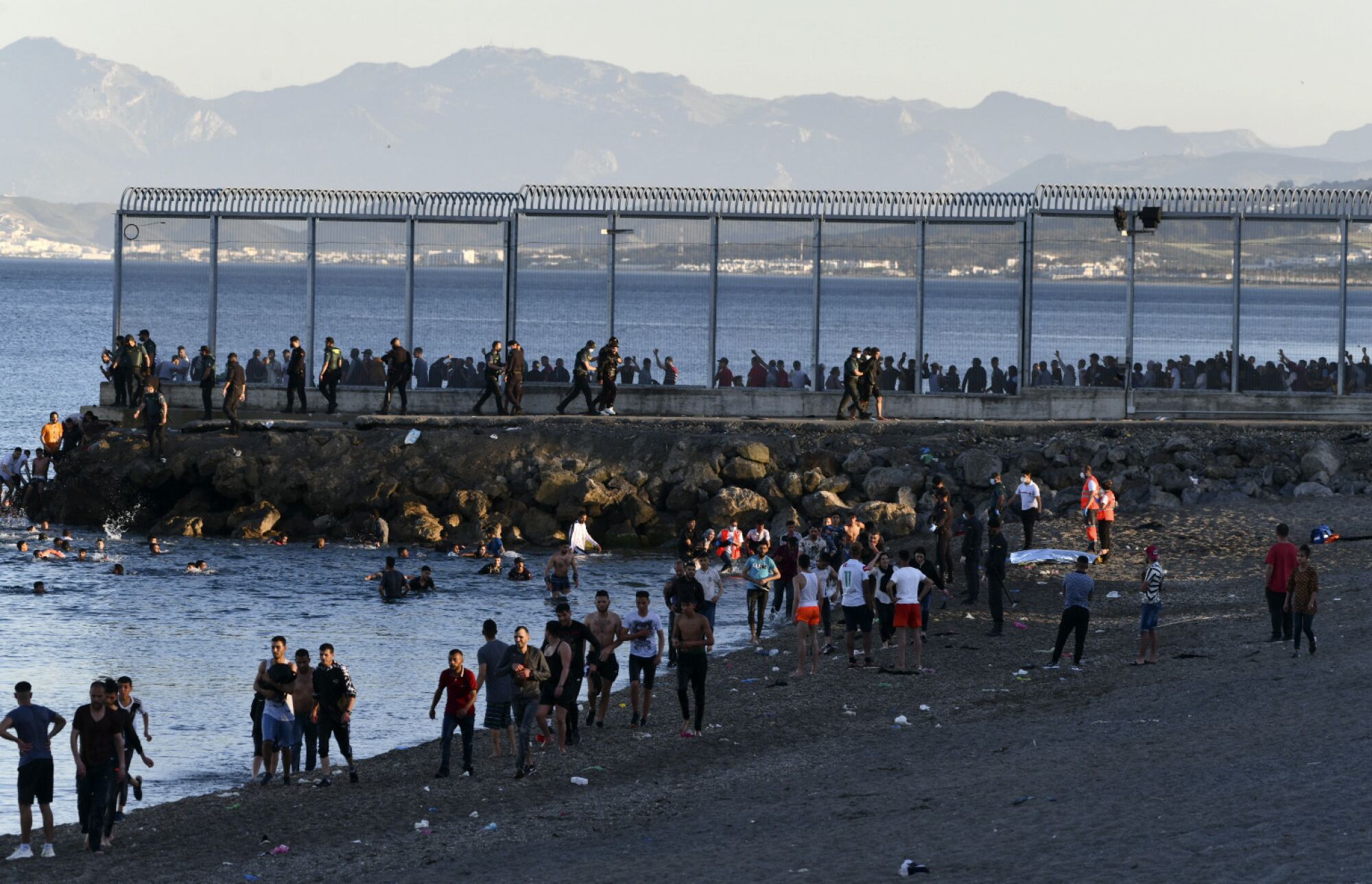 Scores of migrants walk and swim around a border fence that extends into the sea