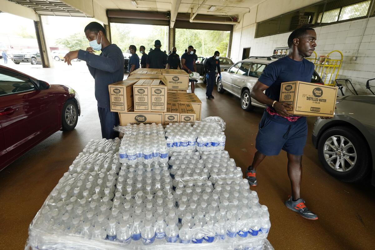 Firefighters and recruits carry cases of bottled water to residents' vehicles.