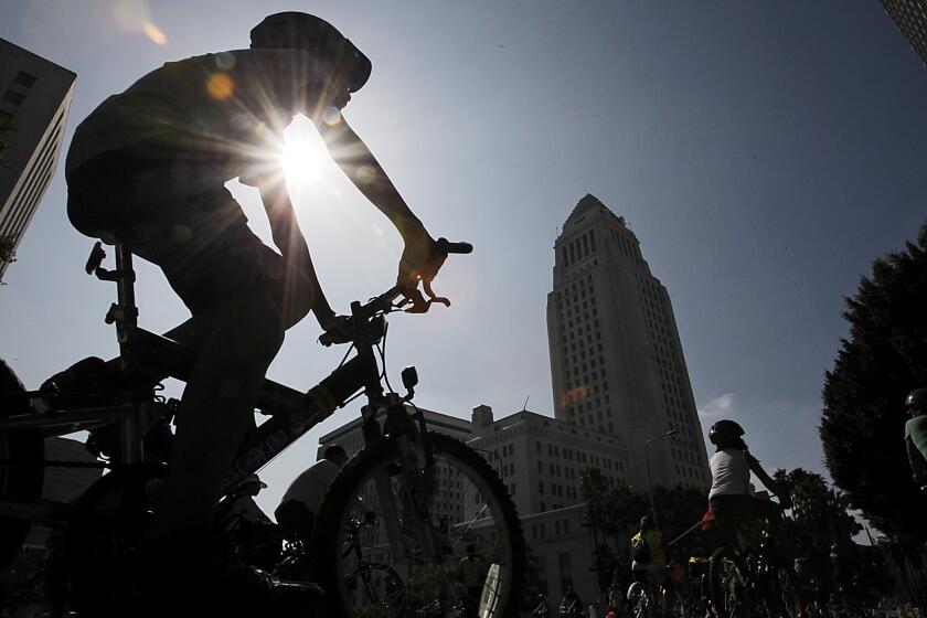 A cyclist wearing a helmet rides past Los Angeles City Hall in 2012.