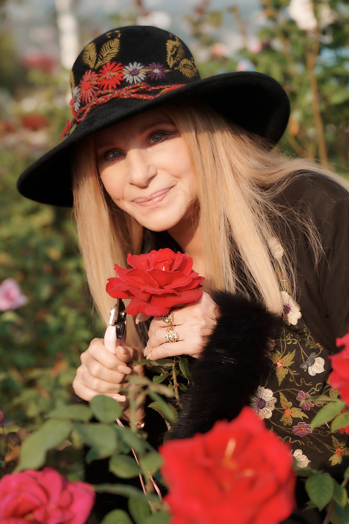Barbra Streisand holds a rose as she stands outside in a garden.