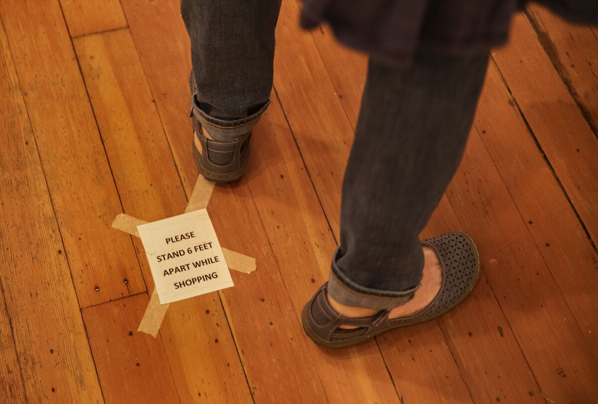A sign on the ground reminds people to observe social distance rules while shopping at a Grass Valley store.