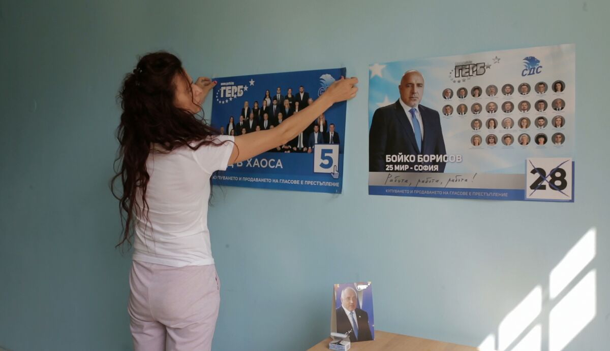 A supporter of former Prime Minister Borissov's GERB political party displays party election posters on a wall, in an office in Sofia suburbs, Tuesday, July 6, 2021. Voters are going to the polls in Bulgaria for the second time in three months this weekend after no party secured enough support in an April 2021 parliamentary election to form a government. Former three-time Prime Minister Boyko Borissov’s GERB party performed best in the inconclusive election, but it received only 26 percent of the vote. Polls suggest a neck-to-neck race between Borissov’s party and its main rival, the anti-elite There is Such a People, which is led by popular TV entertainer Slavi Trifonov. (AP Photo/Valentina Petrova)