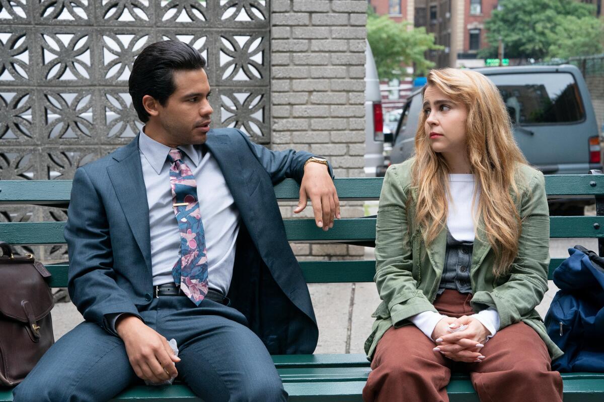 A man and a woman talk while sitting on an outdoor bench.