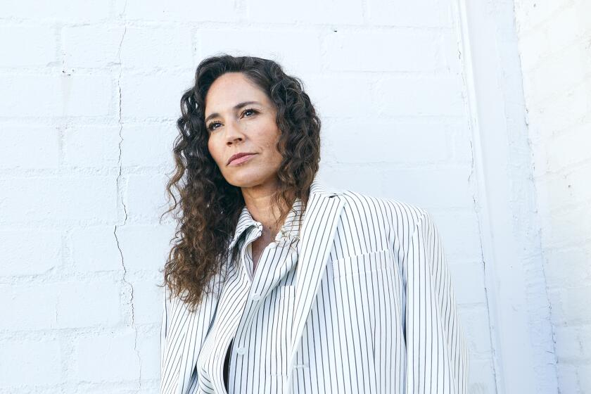 Sue Bird in a white and black pinstripe suit in front of a white brick wall