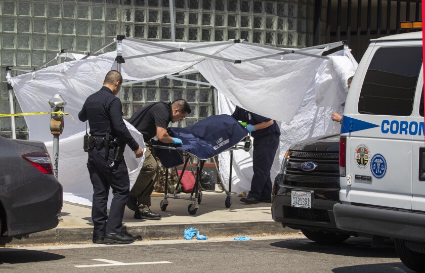 An LAPD officer assists as investigator Adrian Munoz, center, of the L.A. County coroner’s office, removes the body of Alvin Robinson near the intersection of Massachusetts Avenue and Sepulveda Boulevard.