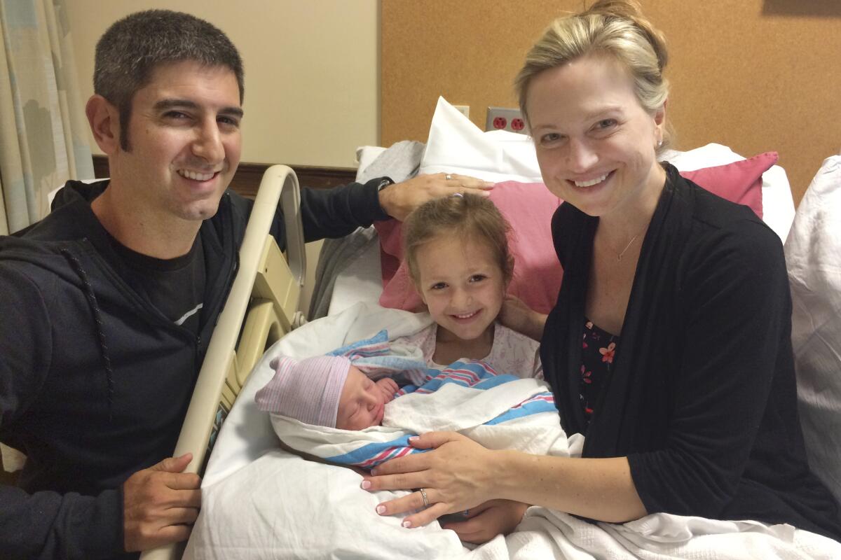 A couple with a newborn baby and a girl in a hospital room