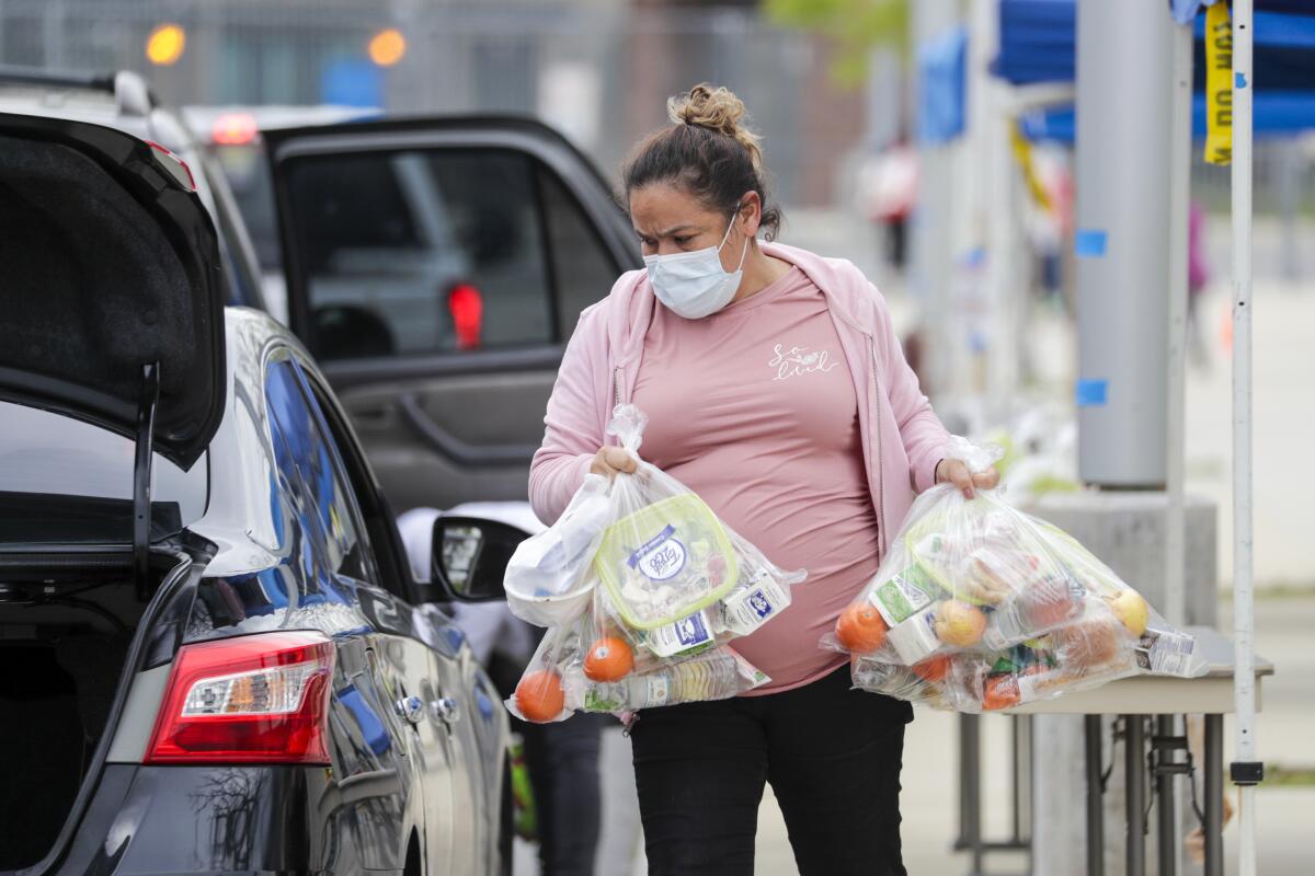 A woman carries bags of food to a car