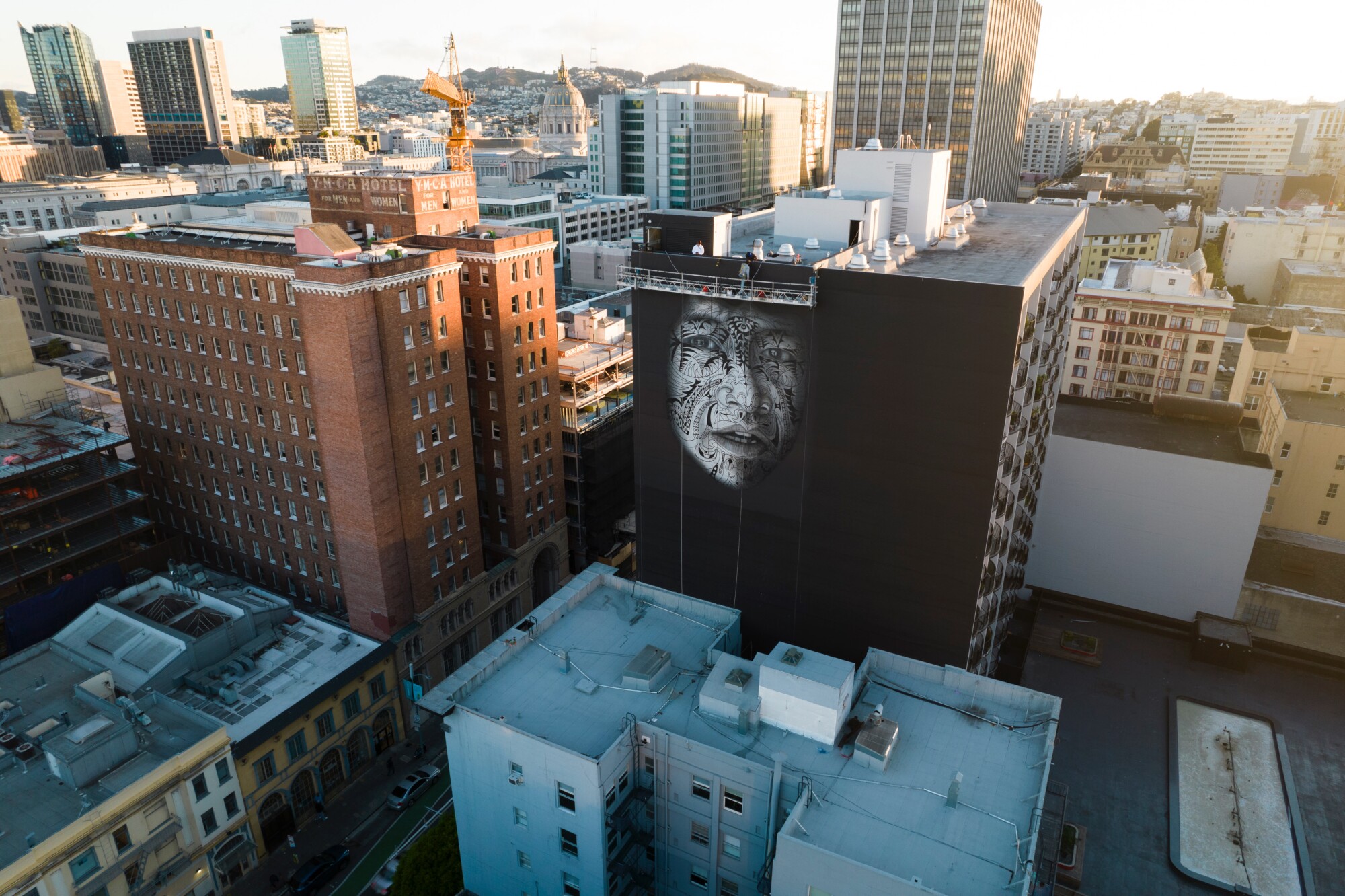 An aerial view shows a building facade painted black, from which emerges a tattooed face — from a work by Carlos Villa.