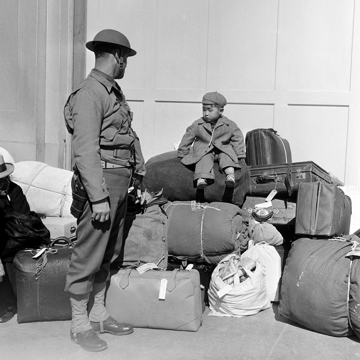 A military policeman watches a boy sitting on a pile of baggage in San Francisco in 1942.