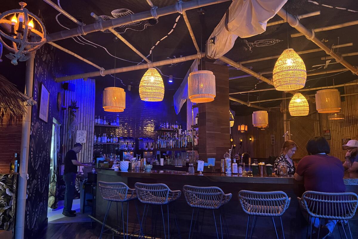 The bar at Broken Compass Tiki with wicker barstools and wicker lights hanging from the ceiling