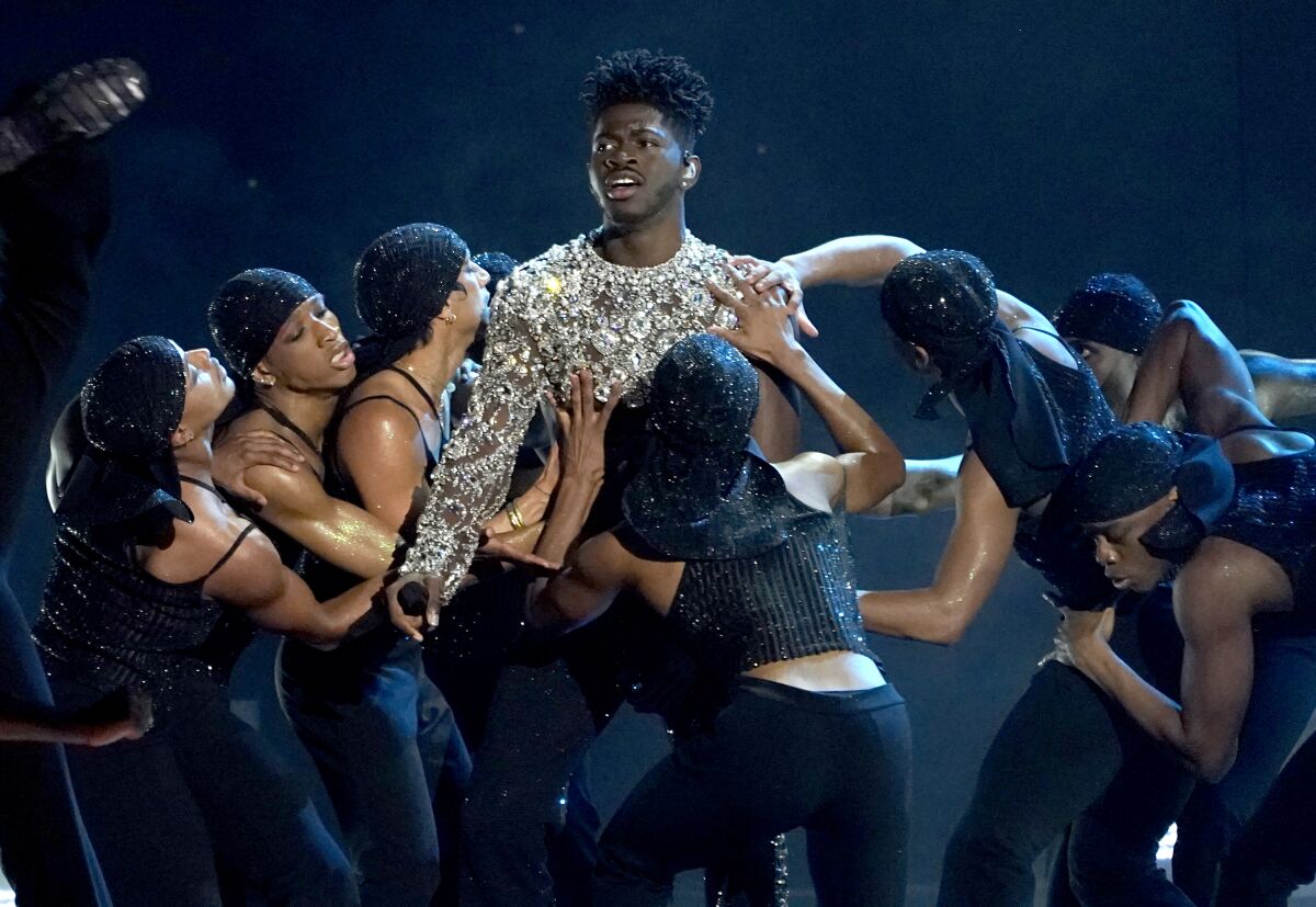 A man is surrounded by dancers fawning over him while singing onstage.