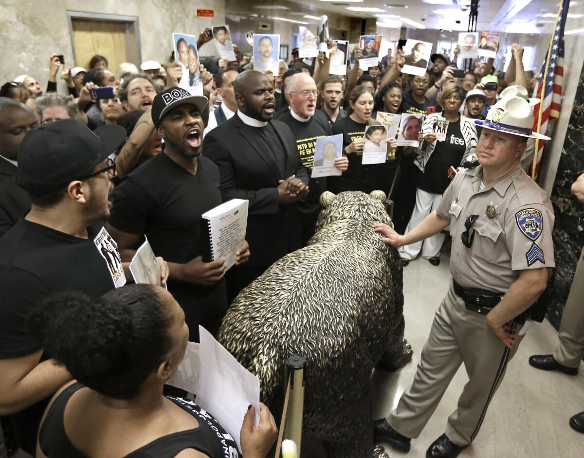 California Highway Patrol Sgt. Steve White, right, stands outside the office of Gov. Jerry Brown as protestors shouting ,"Black lives matter!" block the hallway last month demanding approval of AB 953, a bill aimed at reducing racial profiling by the police.