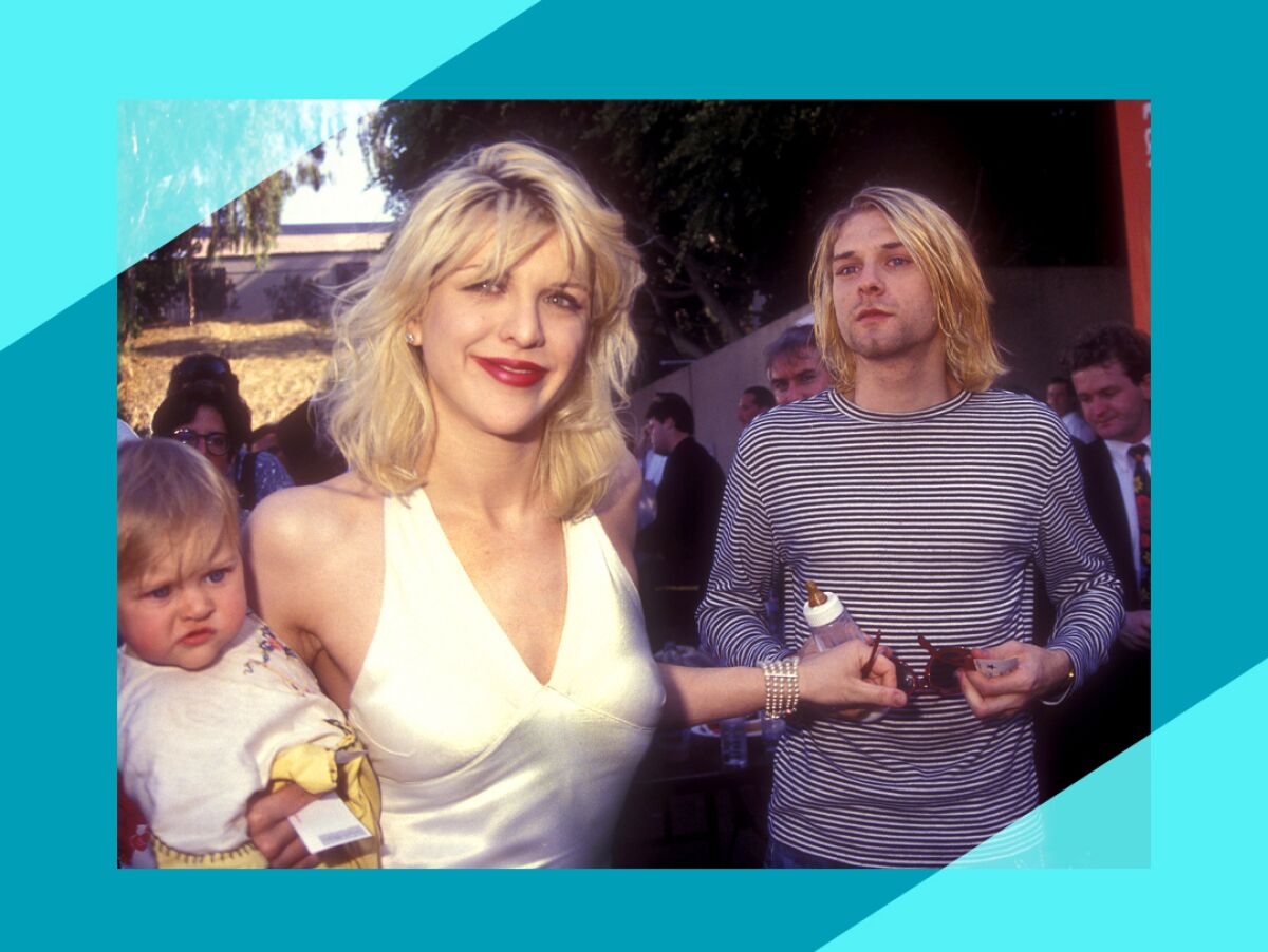 Courtney Love stands next to Kurt Cobain and smiles at the camera while holding their baby daughter.