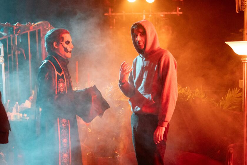 A man in white face paint consults with a director in a hoodie.