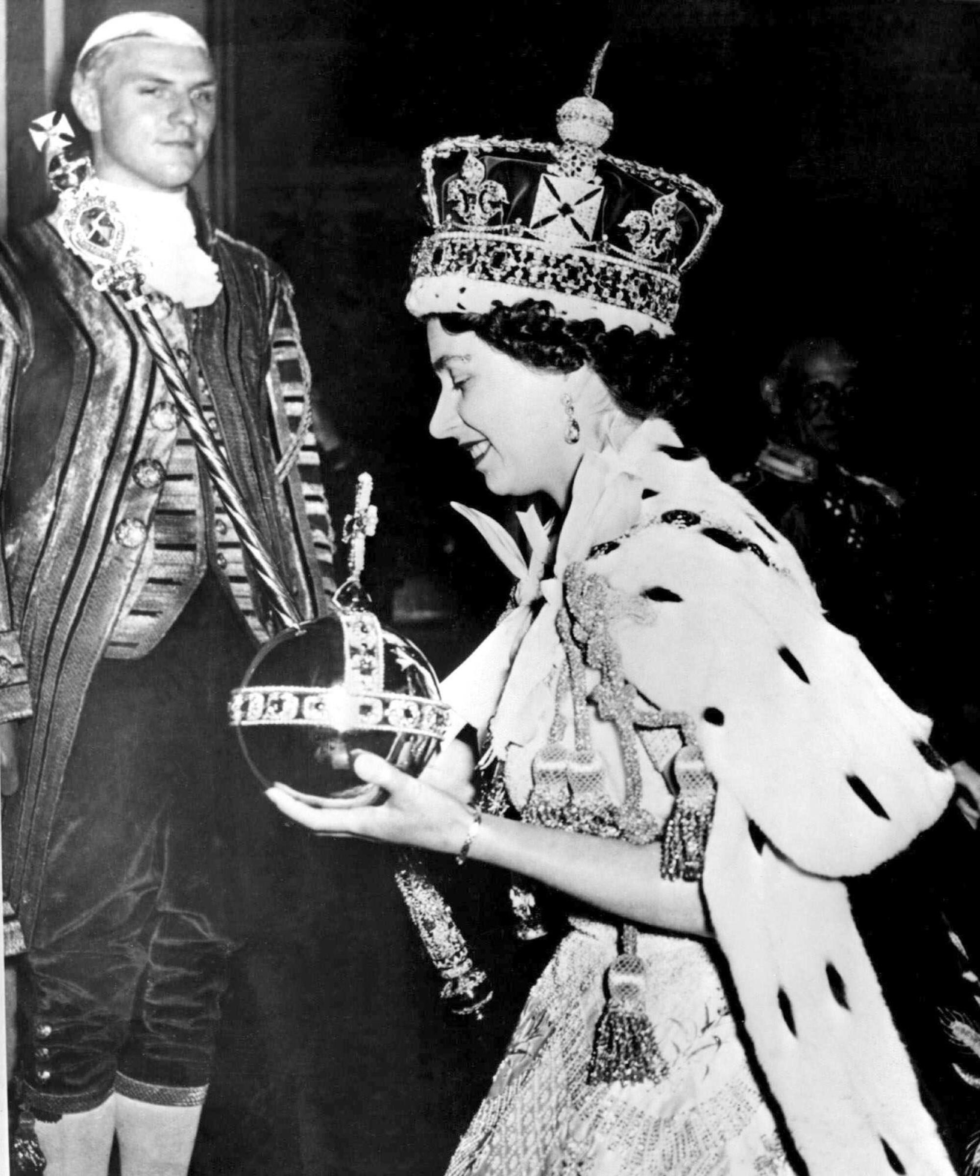 Queen Elizabeth II in a black-and-white photo wearing a large crown and carrying the Orb and Scepter