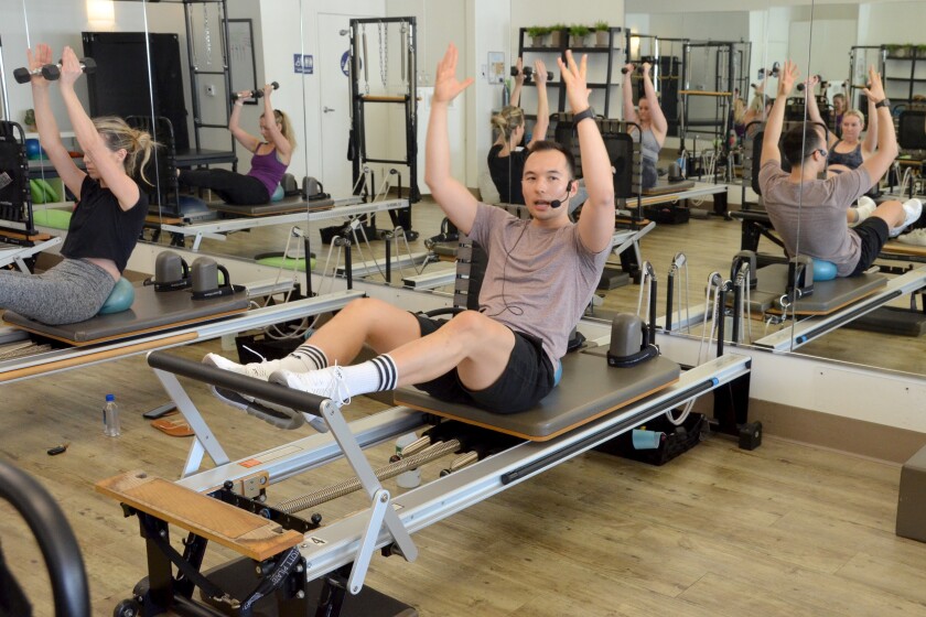 Core Reform Pilates Newport Beach instructor Chad Balen demonstrates a seated abdominal exercise using hand weights and ball.