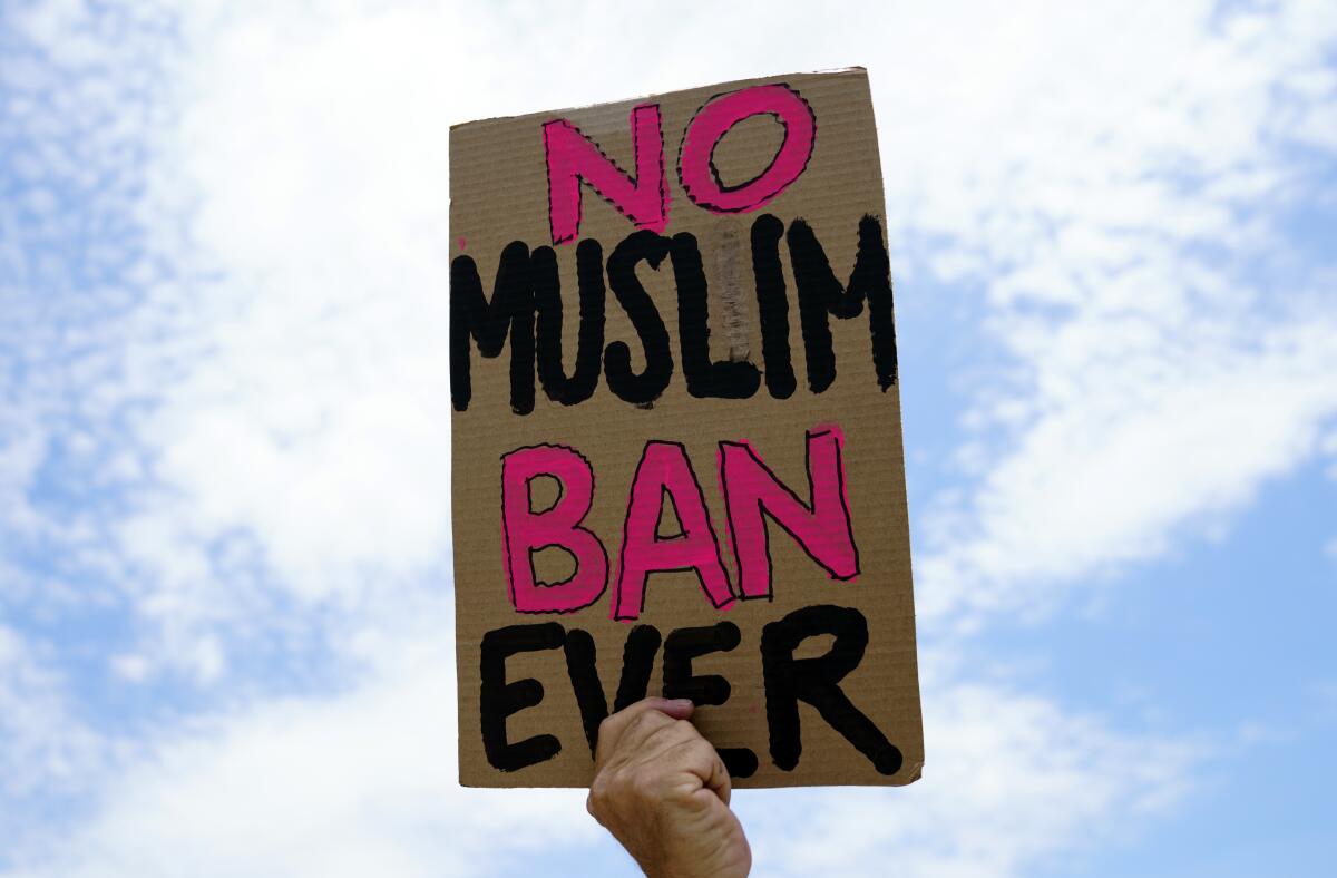 A protester holds up a hand-painted cardboard sign that reads "No Muslim Ban Ever"